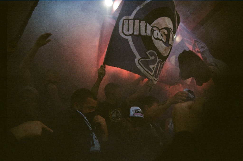 A lively crowd of sports fans waving flags amidst smoke, creating an intense atmosphere.